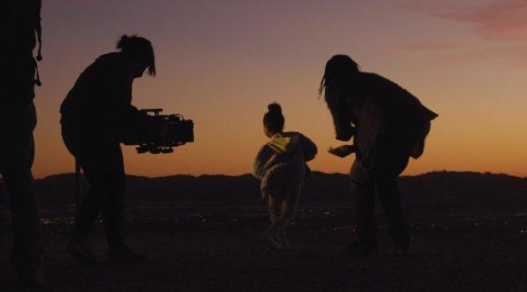 A behind the scenes image of a commercial, showing a videographer, director, and actor.